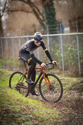 A cyclist wearing a black suit with a number 3 on the back and a blue helmet riding his bike.