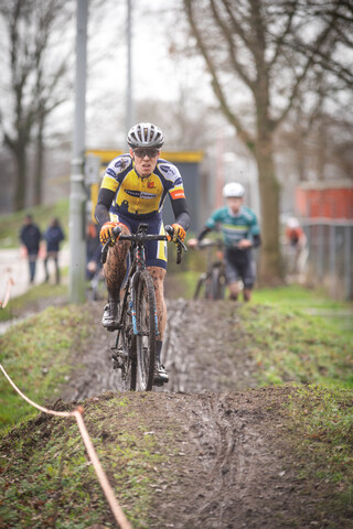 Three cyclists race down a muddy hill as spectators watch from the sidelines.