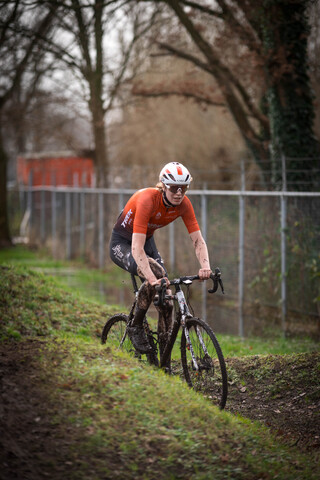 A man wearing a white helmet is riding a dirty black mountain bike.