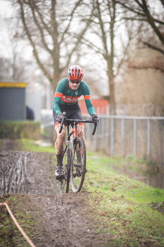 A man in a green and red shirt rides a bike down a muddy hill.