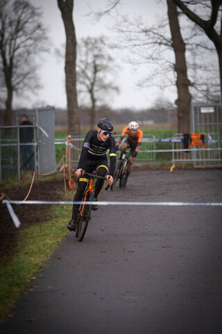 Cyclists on a track with barriers in the background, one rider is wearing a black helmet.