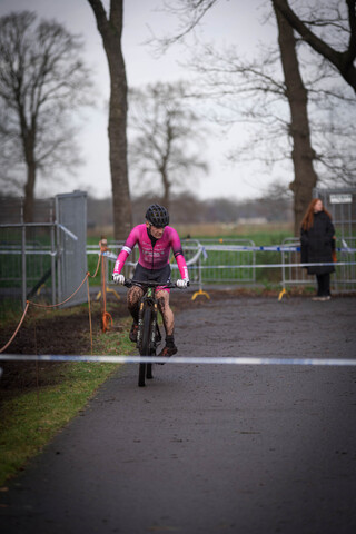 A cyclist with pink and black clothing riding a bicycle in a Cyclocross event.