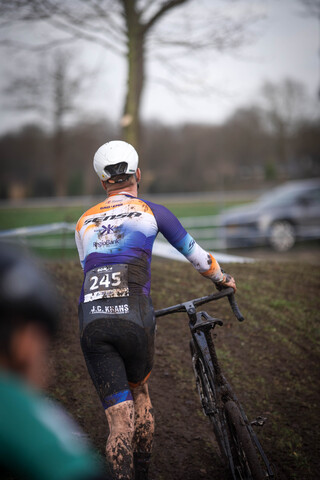 A person riding a bike in the rain. They are wearing number 245 and their shirt says Cyclocross.