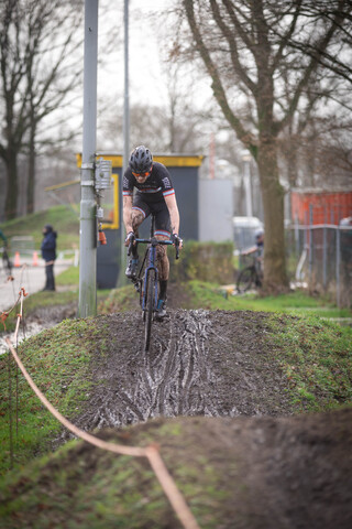 A bicyclist in a black jersey is riding through muddy water.