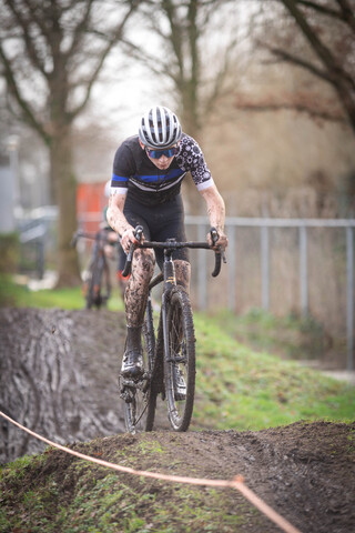 A person riding a mountain bike on dirt. They are wearing a black and white jersey, gloves, and a helmet.