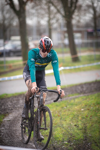 A person in a red helmet rides a bike through mud on the track of the Cyclocross.