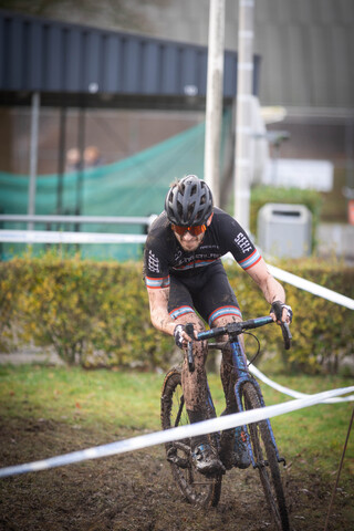 A man is riding a bike in the dirt with a green tent and fence behind him.