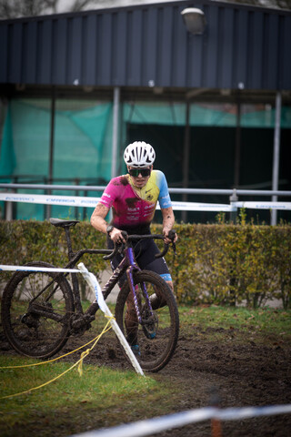 A man in a pink and blue shirt is riding a bicycle with a white helmet on.