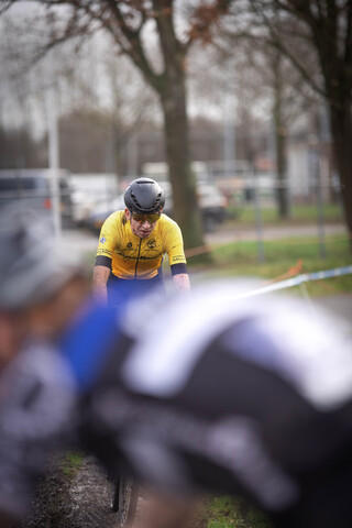 A group of cyclists compete in a race, with one man wearing an orange jersey.