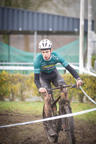 A person wearing a helmet rides a muddy bicycle on a track.