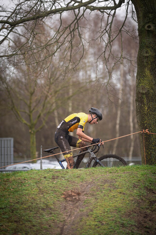 A cyclist wears a black and yellow uniform and is holding on to a rope.