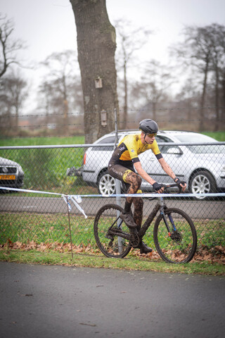 A cyclist is riding in a parking lot with a car directly behind him.