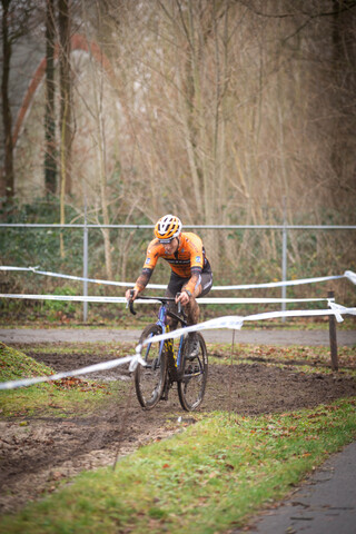 A cyclist wearing a yellow and orange shirt rides through the woods.