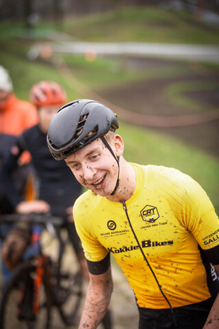 A smiling man wearing a black helmet and a yellow top that says Cyclocross.