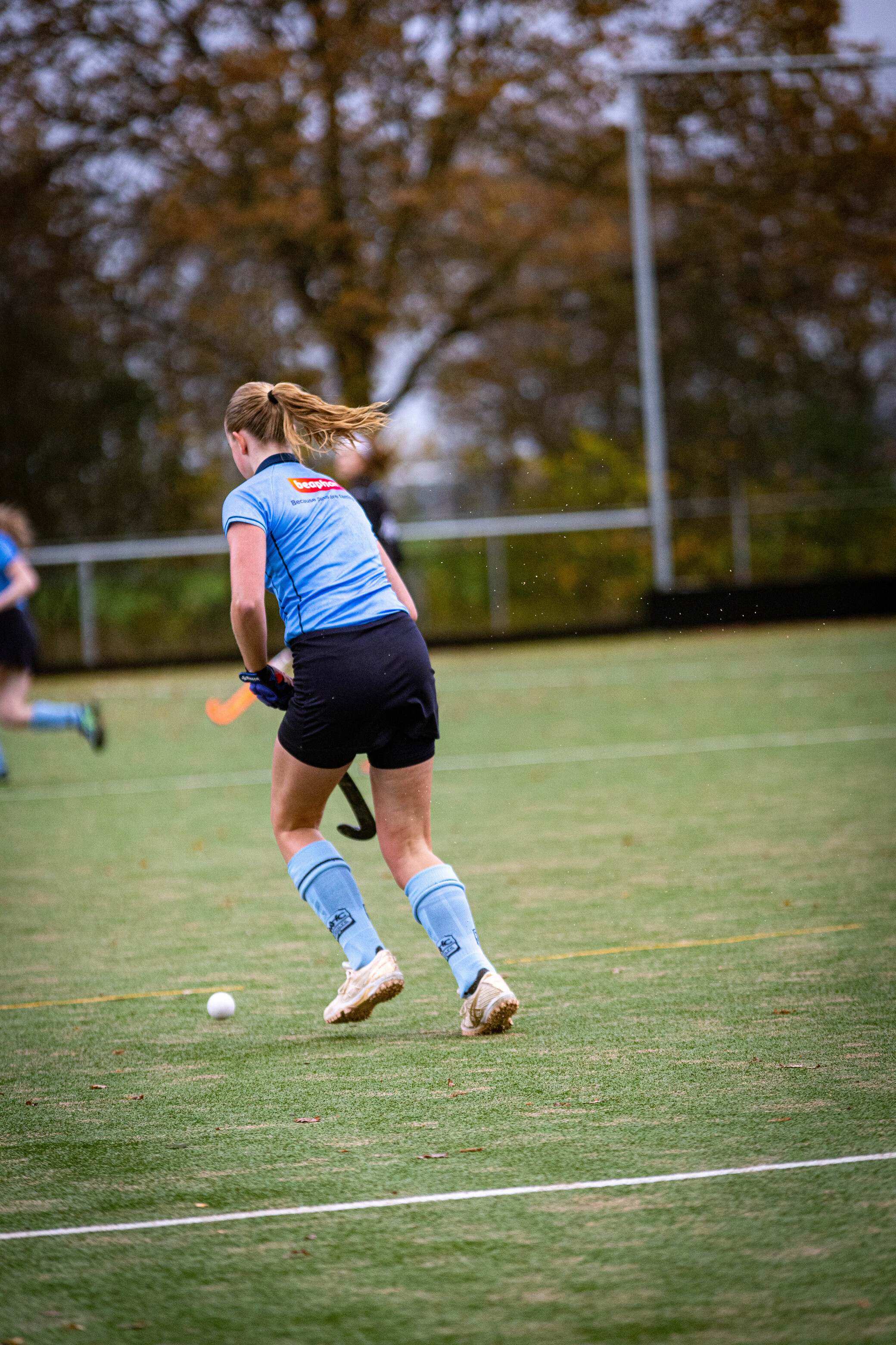 A young woman in a blue jersey and shorts playing hockey.