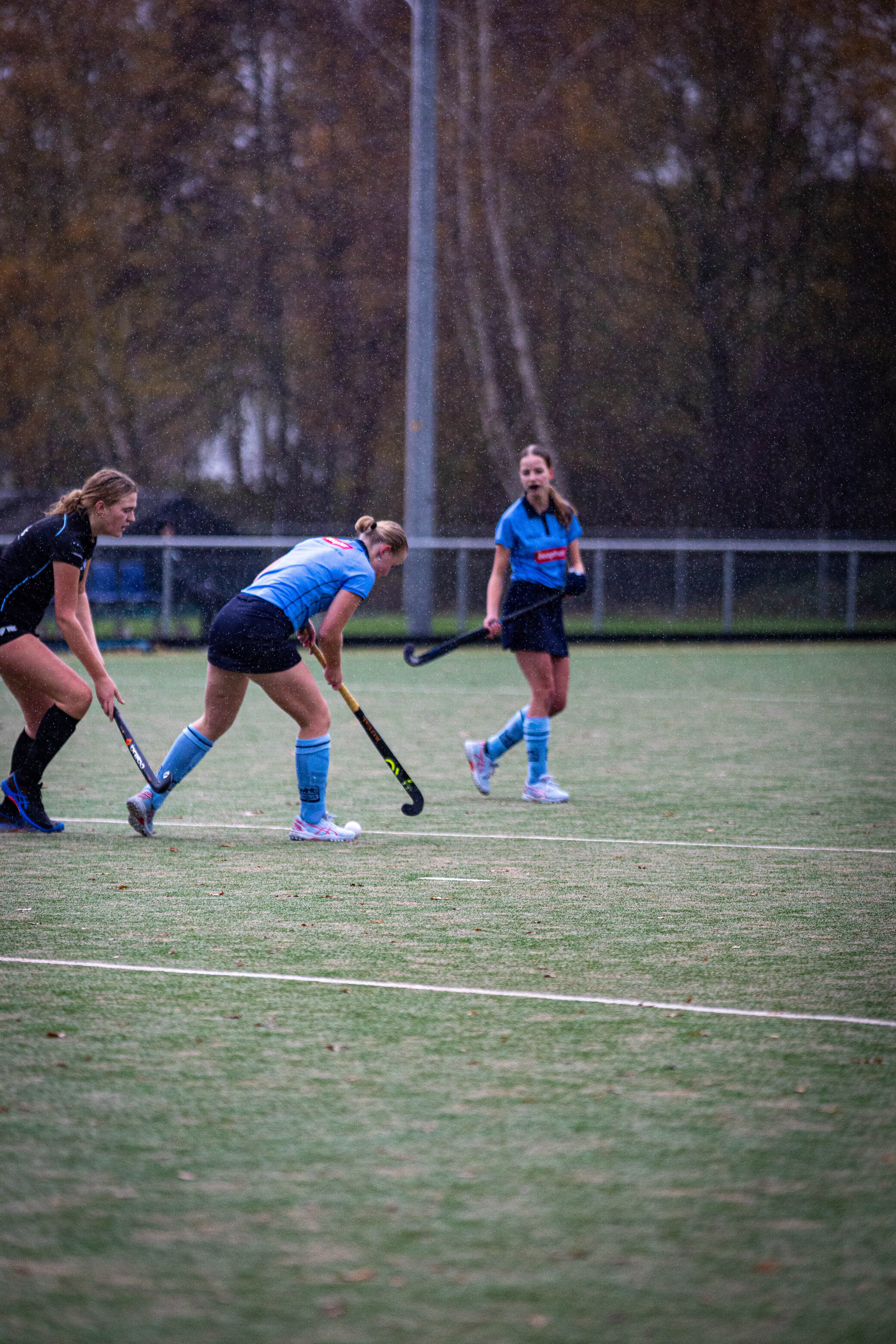 A group of female hockey players, one with her hands on her knees and two others with their sticks.