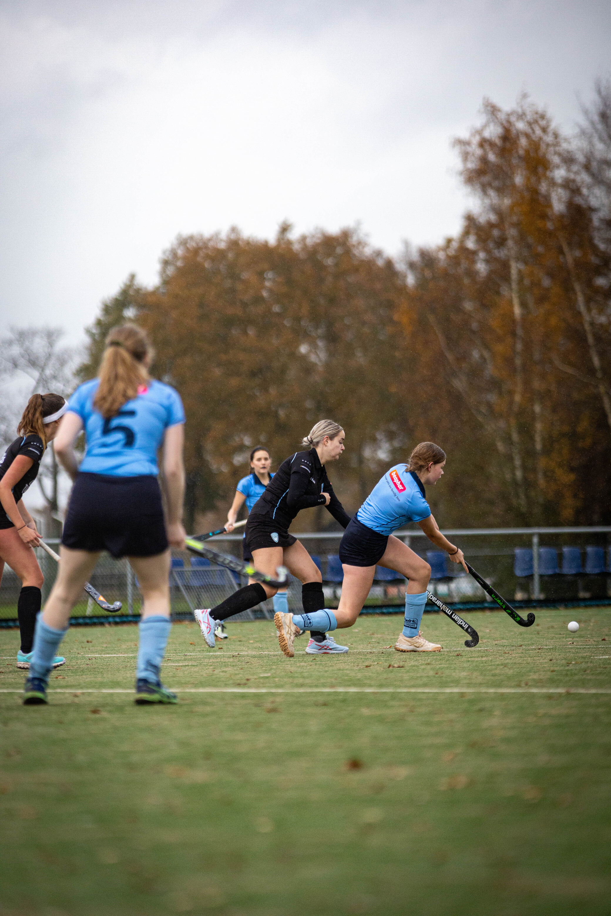 A group of women playing hockey in a park, the player on the right is wearing number 19.