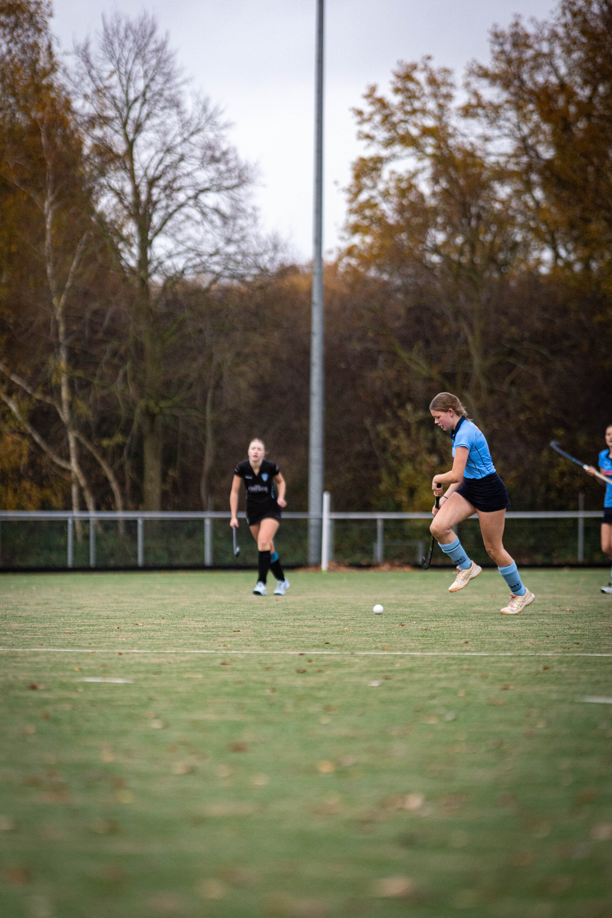 A young woman wearing a blue soccer jersey, kicks a soccer ball with her left foot on a field.