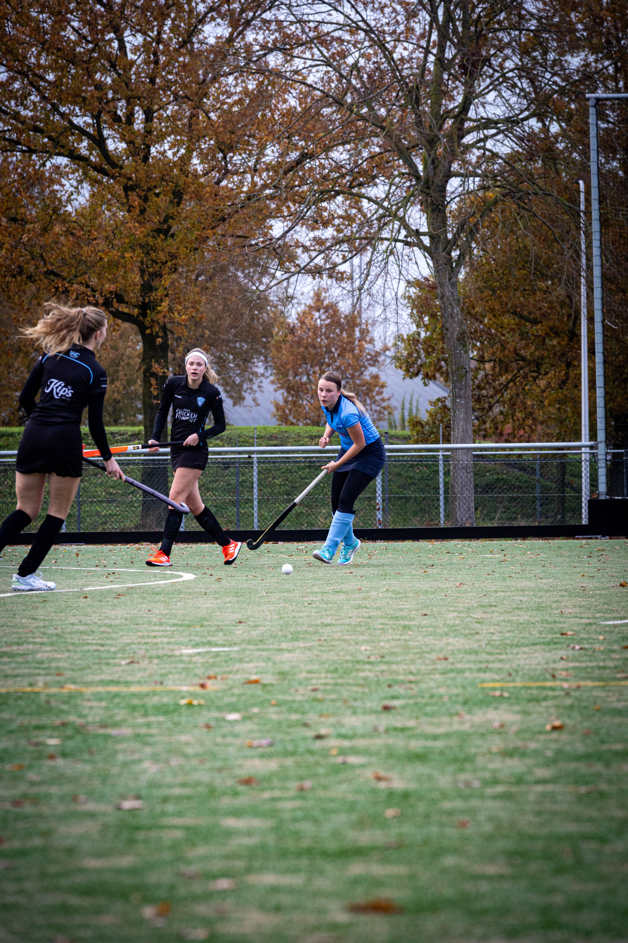 Three women playing a game of hockey on an outdoor field.