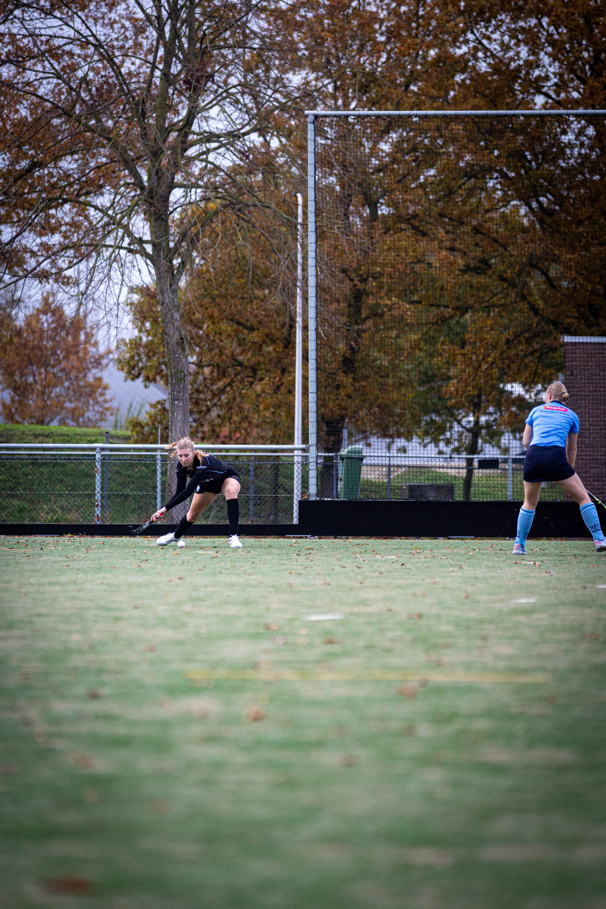 The hockey players are practicing on the field, one of them is wearing a blue jersey and the other is in black.