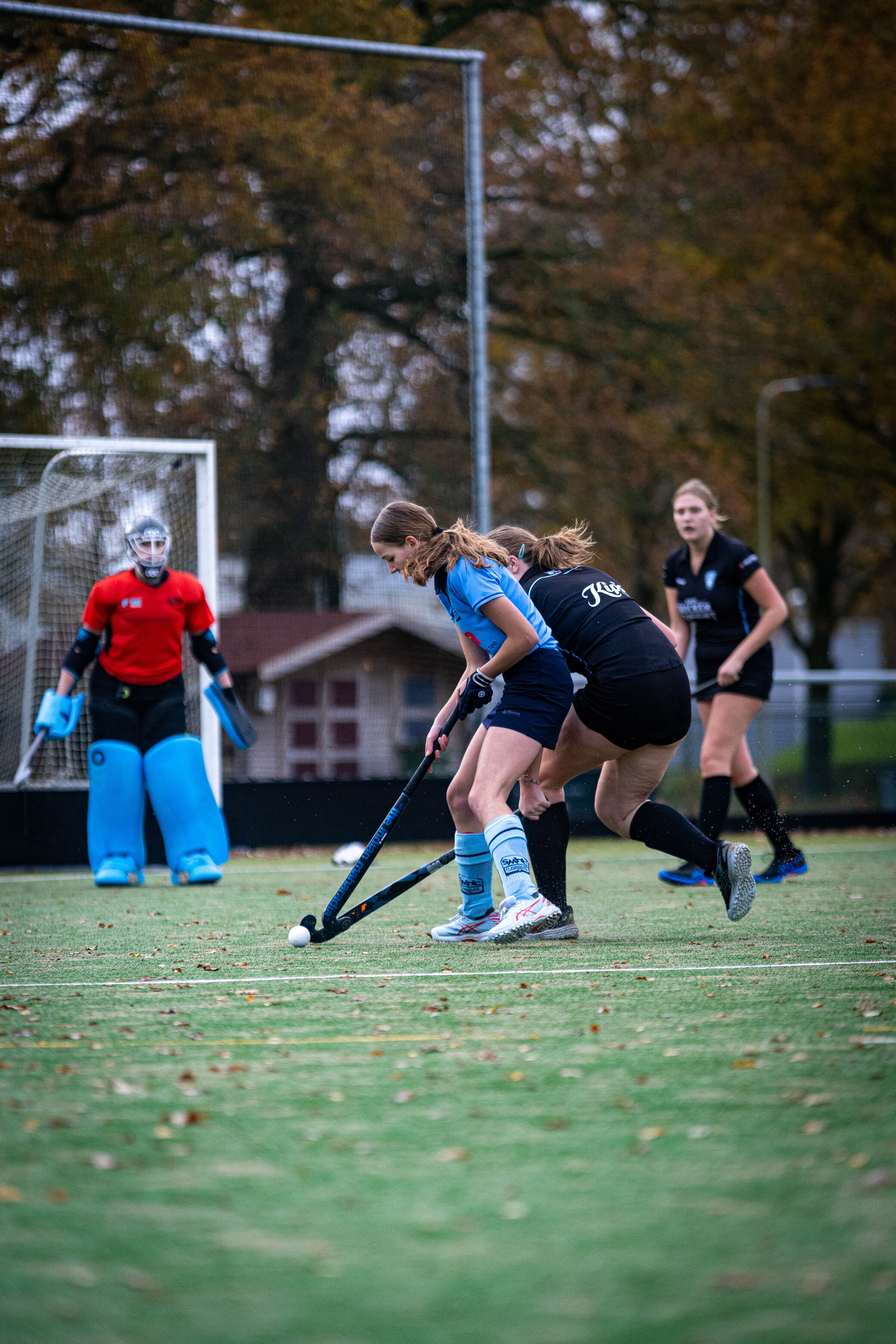 A player wearing a blue jersey on the field with a hockey stick in her hand.