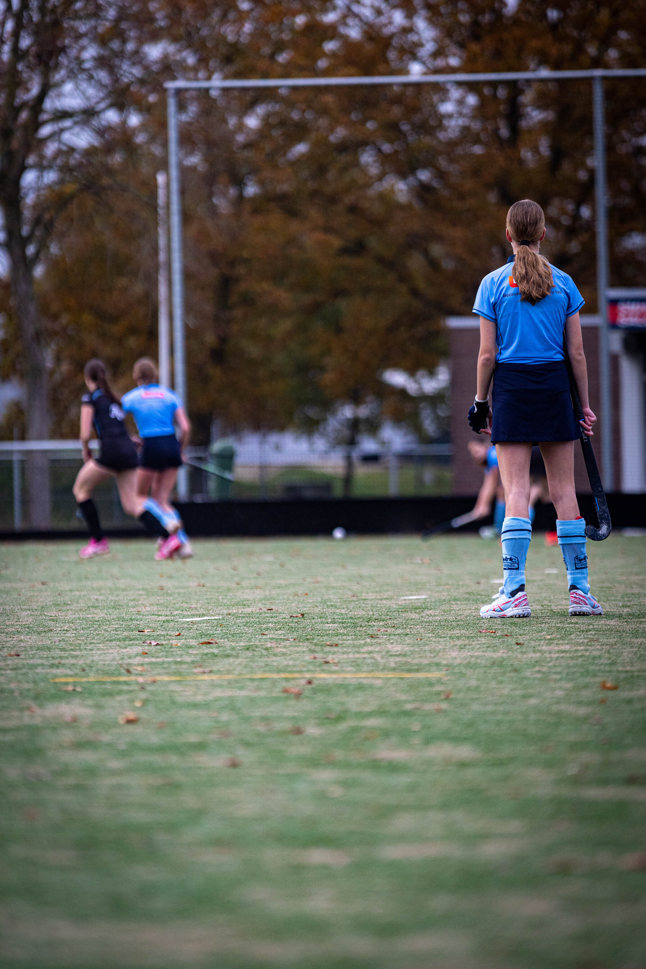 Hockey players in blue uniforms practice on a grass court.