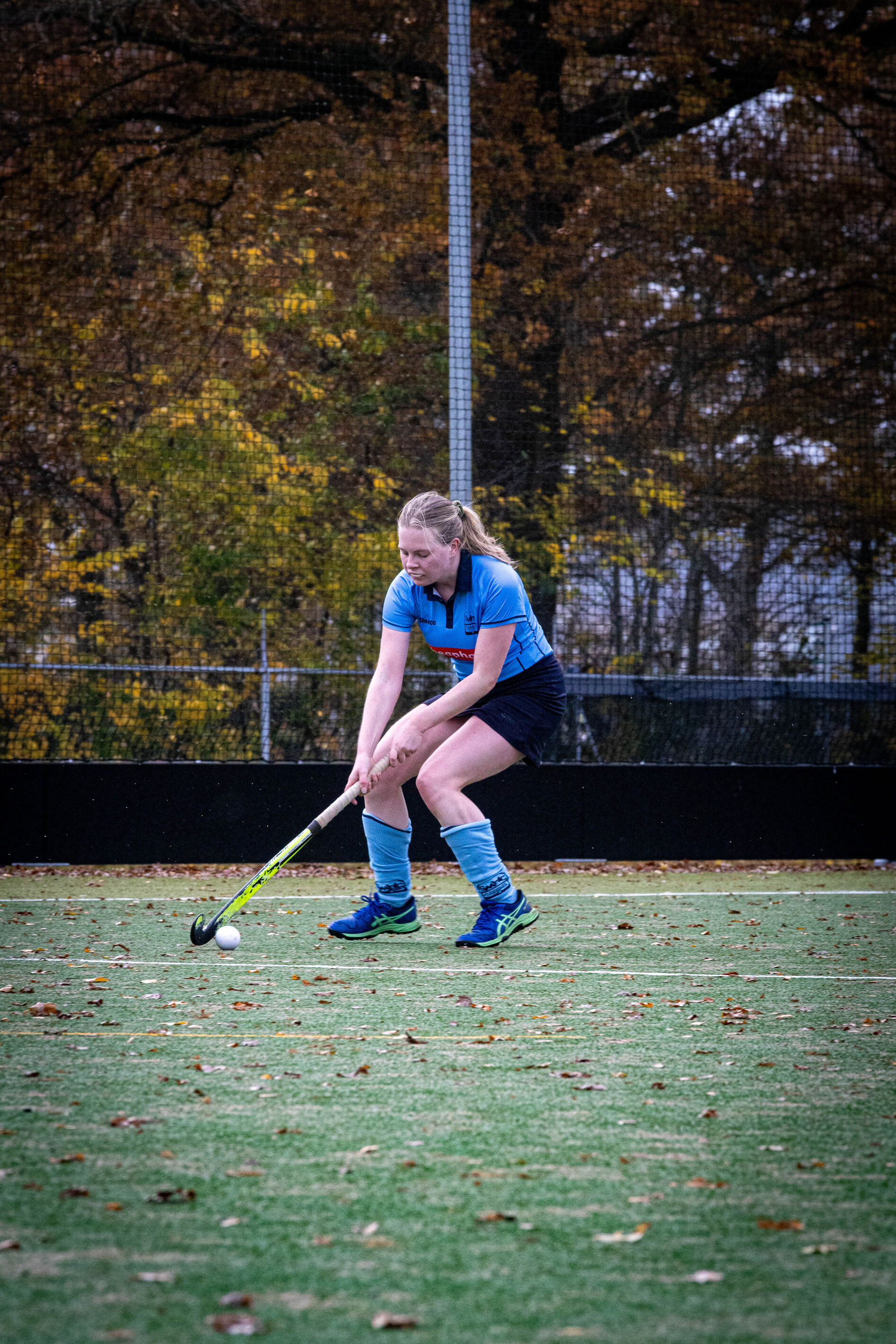 A young girl in a blue shirt and shorts plays field hockey. She's wearing her team jersey with the number 19 on it.