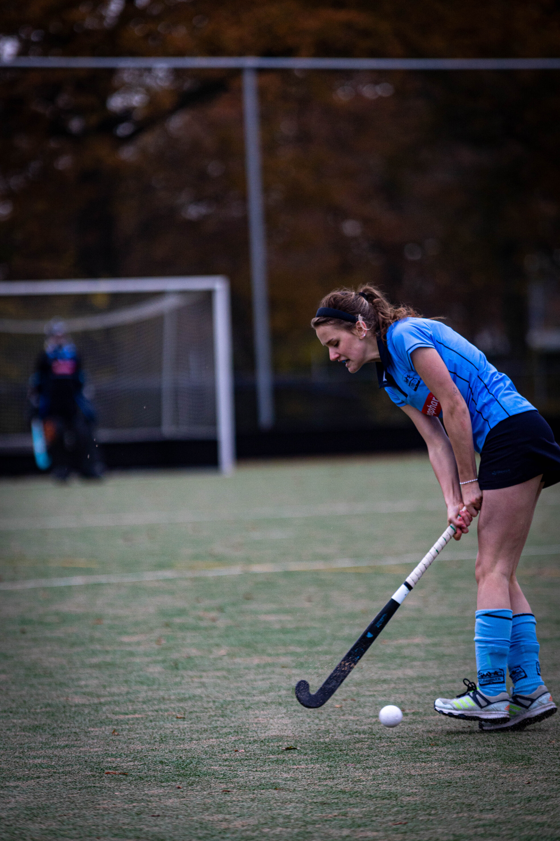 A girl wearing a hockey uniform is getting ready to hit the ball with her stick.