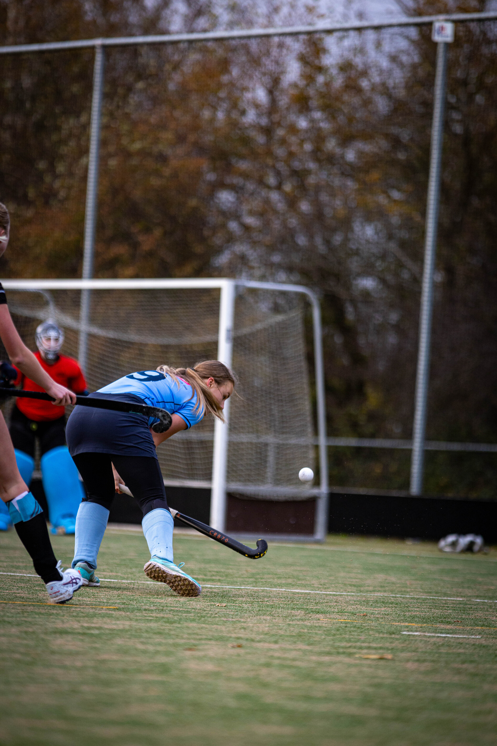 A girl in a blue jersey is about to hit the ball on a field.