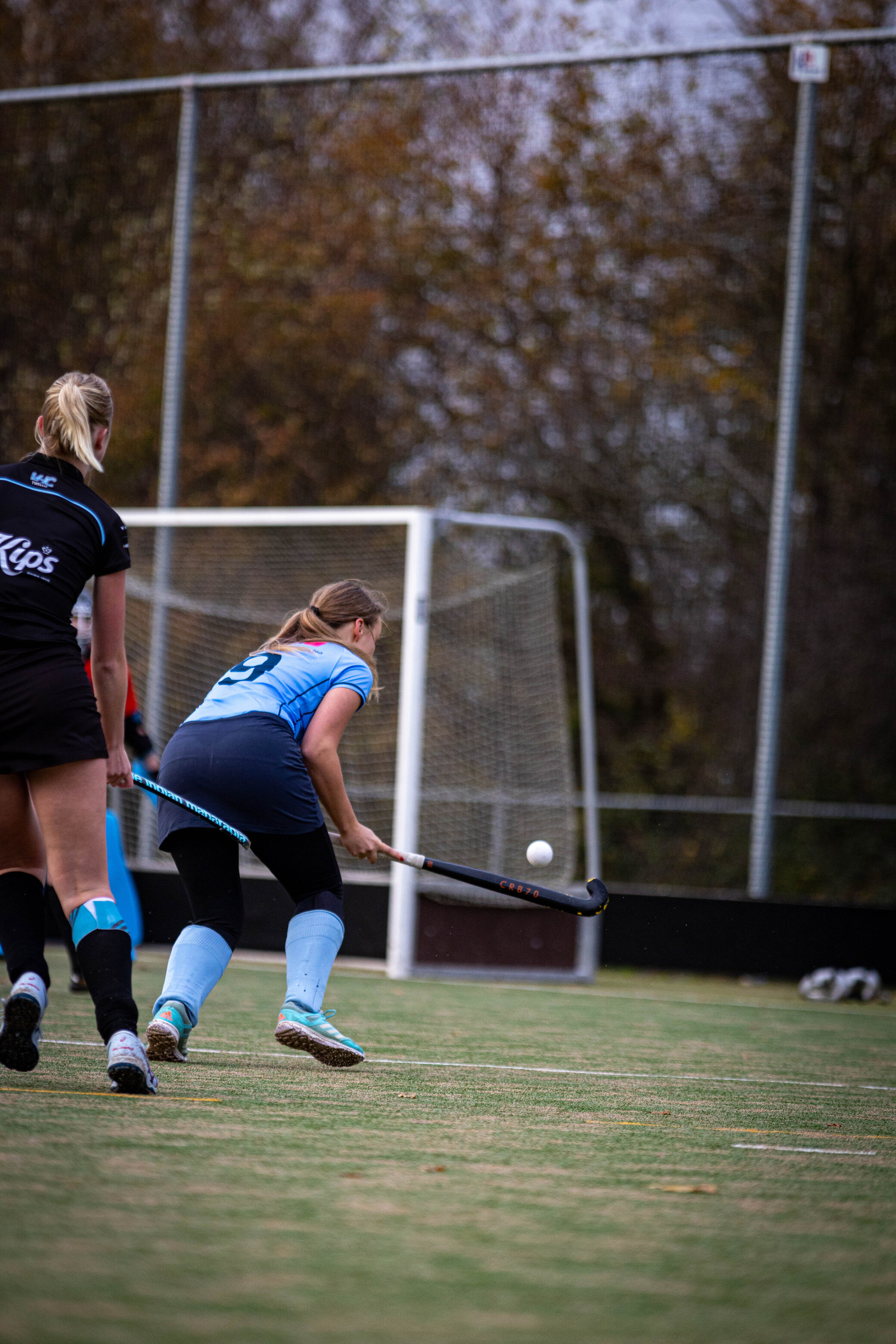 A hockey player in a blue and black uniform is about to hit the ball with her stick.