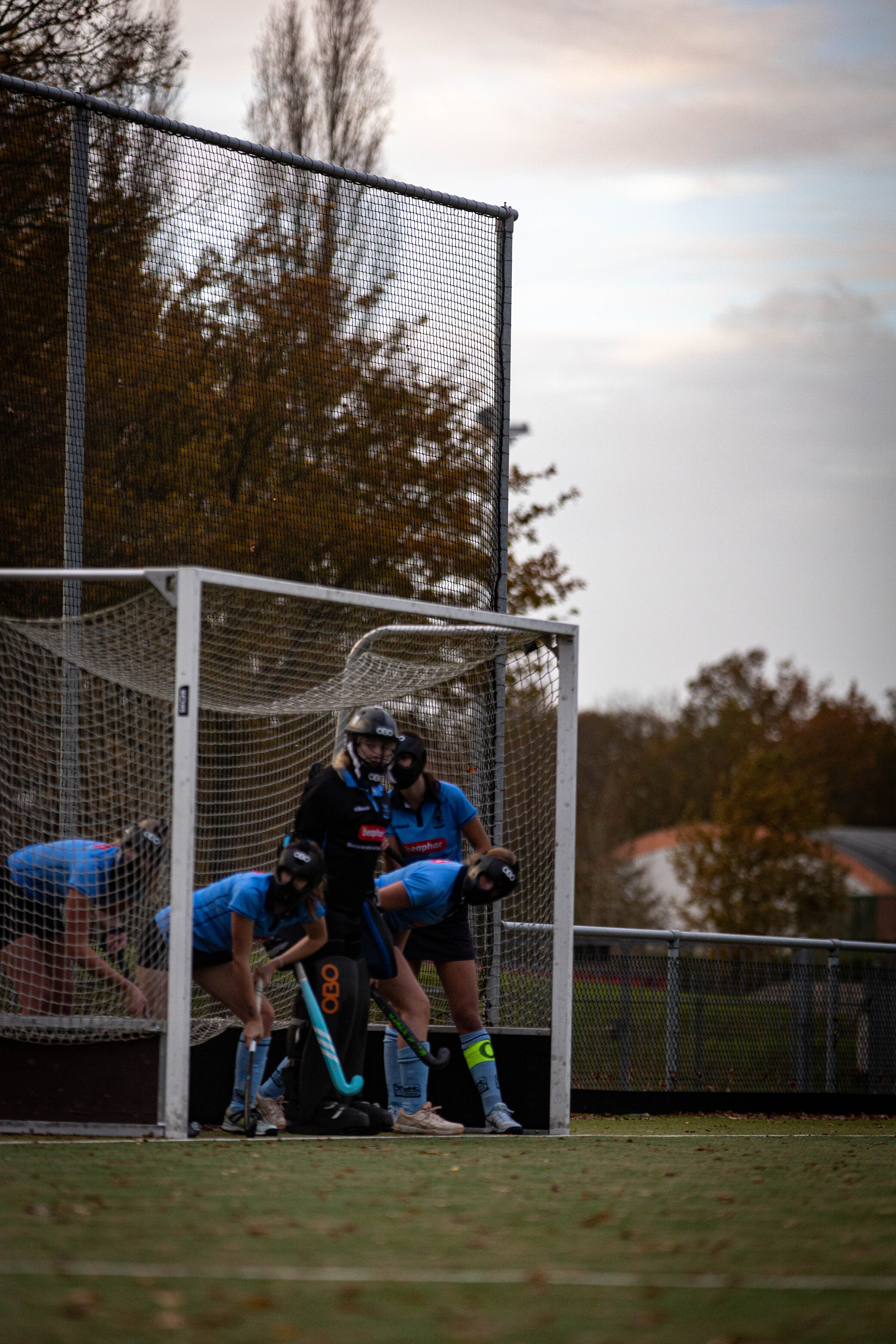 A group of hockey players wearing blue uniforms stand in the goal area at a stadium.