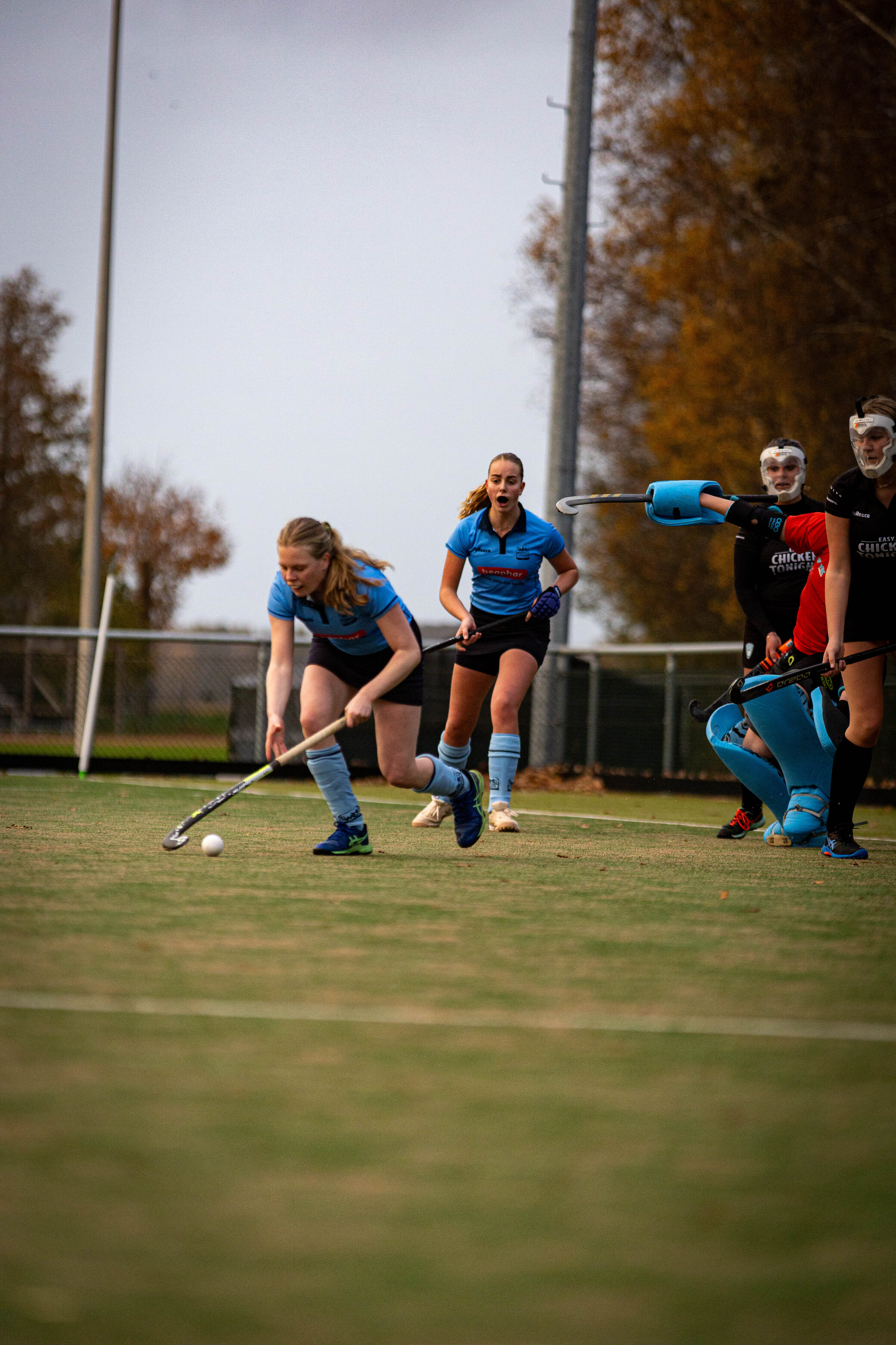 A group of players are on a field with one wearing an orange shirt and a goalie in blue.