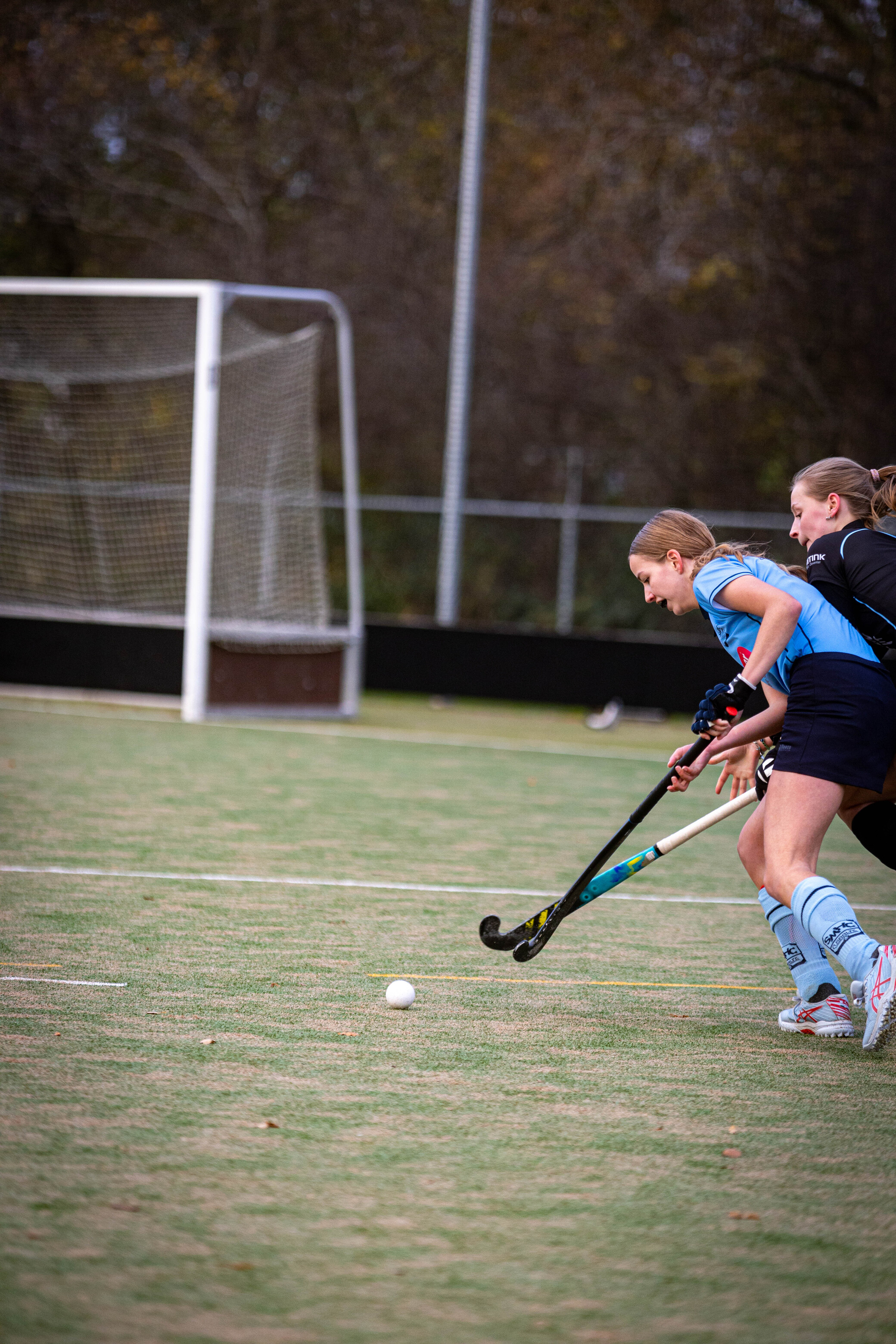 Two girls on a field are about to hit the ball with their hockey sticks.