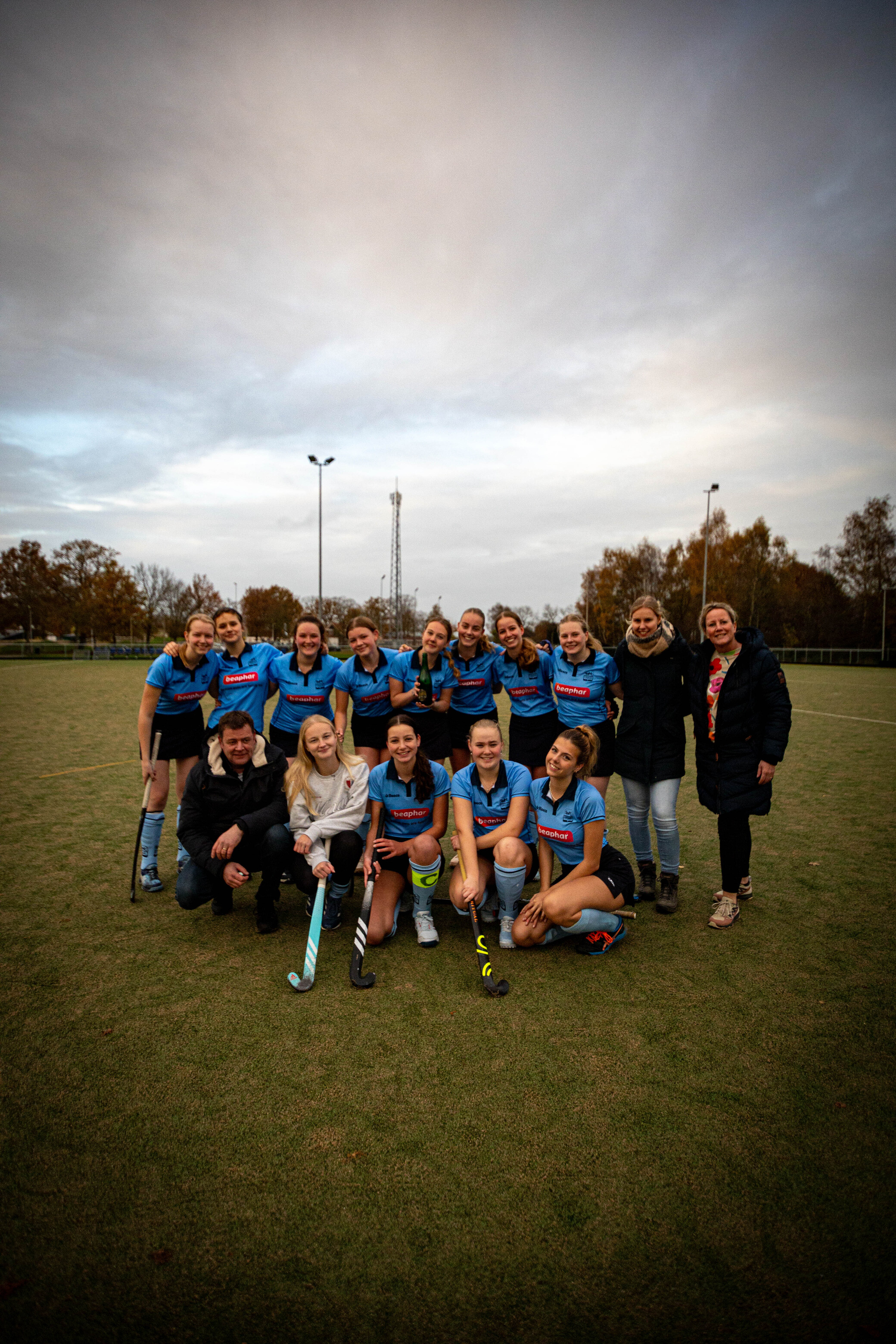 A hockey team celebrates on the field with a coach and their families.