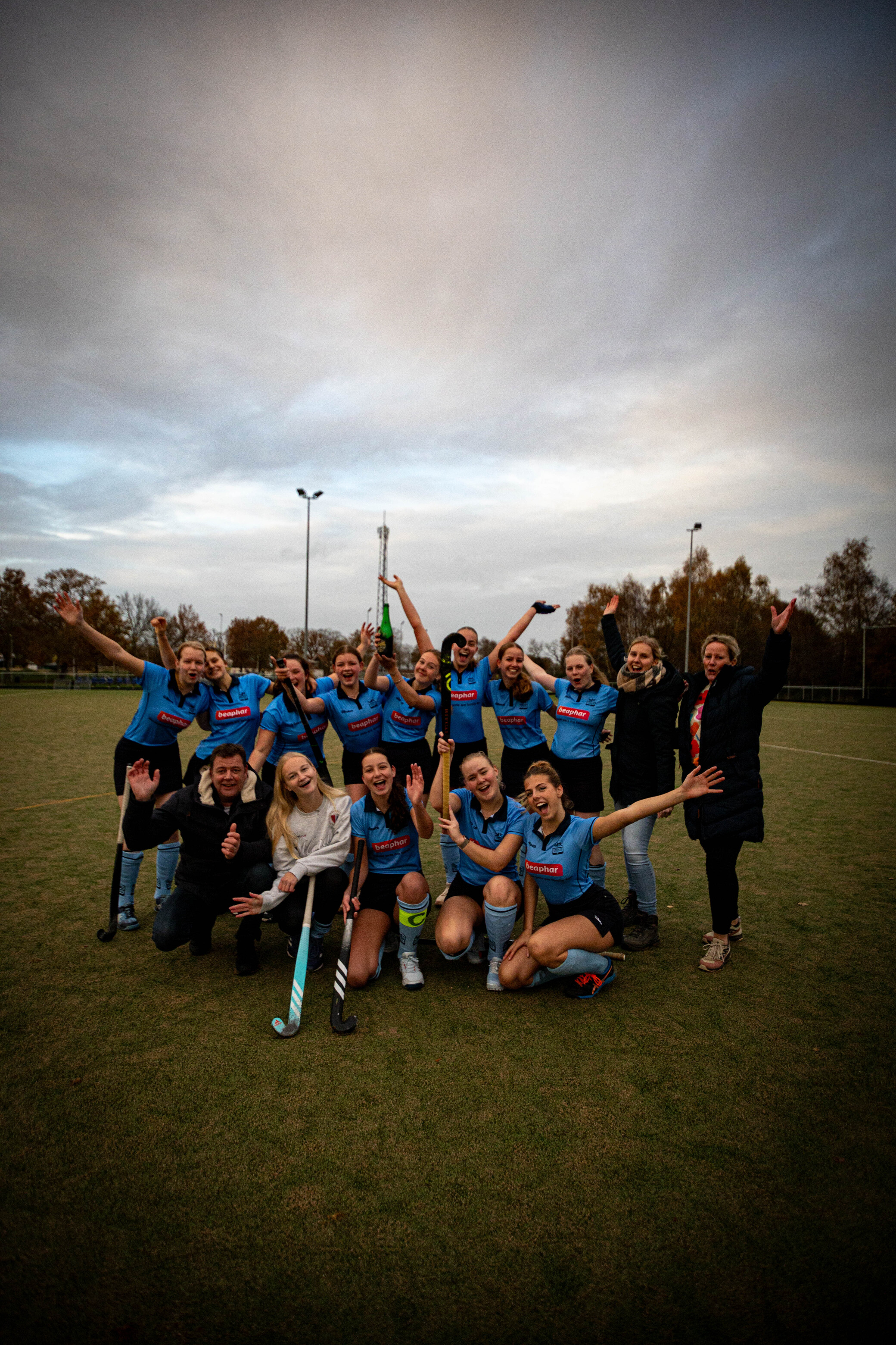 A group of hockey players pose for a photo on a field with a cloudy sky above them.