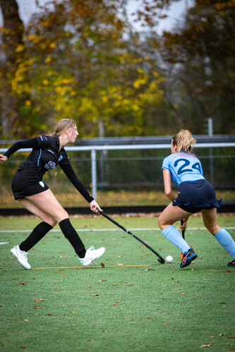 Girls playing hockey on a field with number 24 in blue and 11 in black.