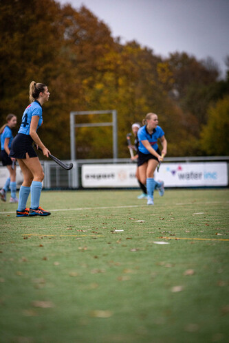 Two girls wearing blue are playing hockey on a field.