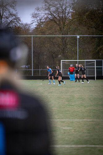 A group of women's hockey players on a field with one wearing black and two others in red.