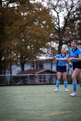 Women play hockey on a field with one of them wearing a SMHC jersey.