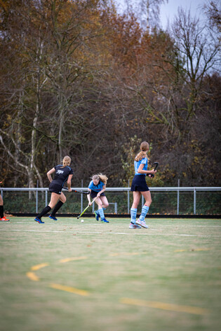 Three women are playing a game of hockey on a field.