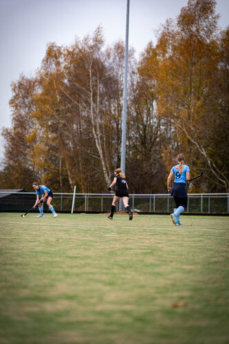 Three people playing hockey on a field in the fall.