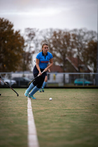 A girl in a blue shirt and black pants is playing hockey, she just hit the ball.