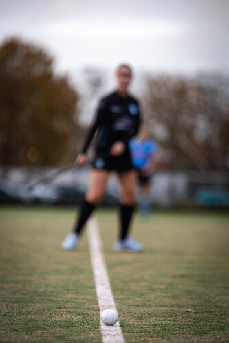 A girl in a hockey uniform stands on the field with her hockey stick held down.