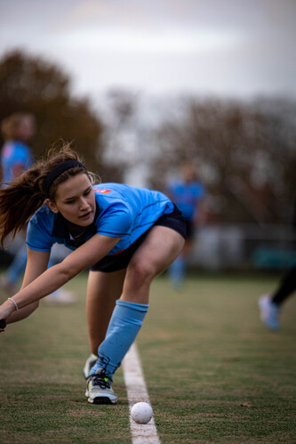 A girl in a blue hockey uniform is bending down to pick up the ball.