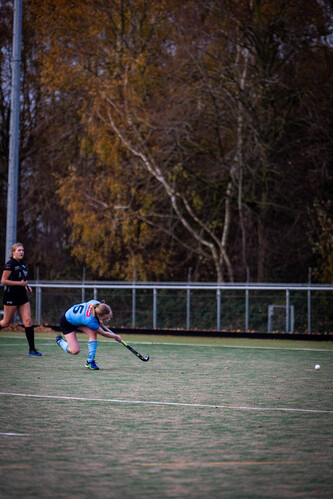 A girl in a blue jersey takes her glove off the ground and hits a hockey ball with her stick.