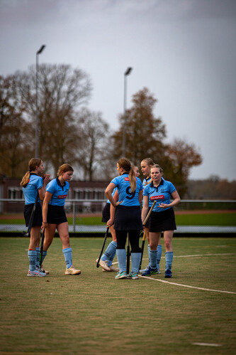 A group of women are standing in a circle on a field wearing blue hockey uniforms.