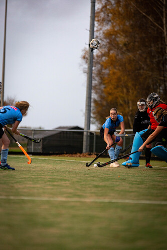 A group of women playing hockey, one in a blue uniform and the other with a black mask.