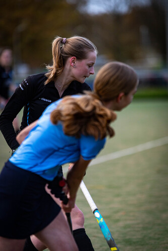 Two young girls on a hockey field, with one holding a hockey stick in her right hand and wearing a blue shirt.