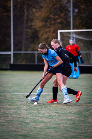 Two girls play hockey on a field near an exit labeled SMHC 19-11.