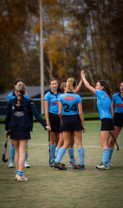 A group of female hockey players high five each other on the field.